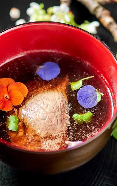 Photo d'un plat cuisiné par Lobna Liverneaux, cheffe de cuisine à Strasbourg. Il s'agit d'un bol rouge avec un bouillon de viande et de pétales de fleurs.